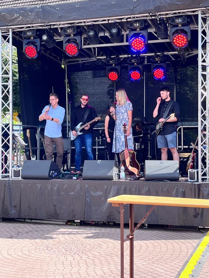 Eine Band probt auf einer Bühne mit rotem Licht, Musiker mit Instrumenten und Mikrofonen.